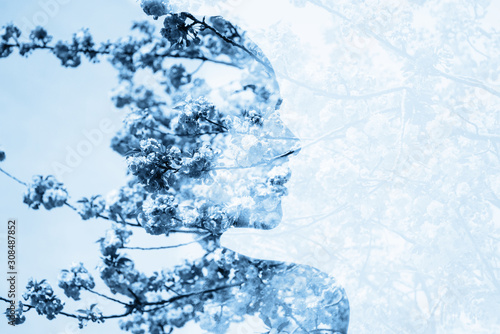 Double exposure photo made with portrait of young beautiful woman and blooming sakura in blue tone.