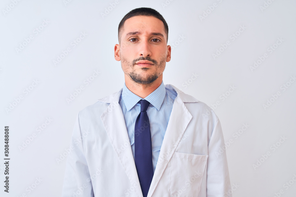Young doctor man wearing white coat over isolated background with serious expression on face. Simple and natural looking at the camera. Young doctor man wearing white coat over isolated background with serious expression on face. Simple and natural looking at the camera.