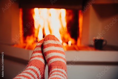 Feet in wool striped socks by the fireplace. Relaxing at Christmas fireplace on holiday evening.