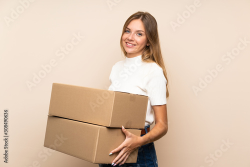 Young blonde woman over isolated background holding a box to move it to another site © luismolinero