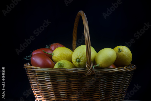 wicker basket with autumn fruits and lemons on black background
