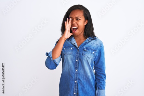 Beautiful young african american woman wearing denim jacket over isolated background shouting and screaming loud to side with hand on mouth. Communication concept.