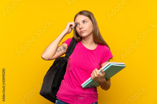Young student girl over isolated yellow background having doubts and with confuse face expression