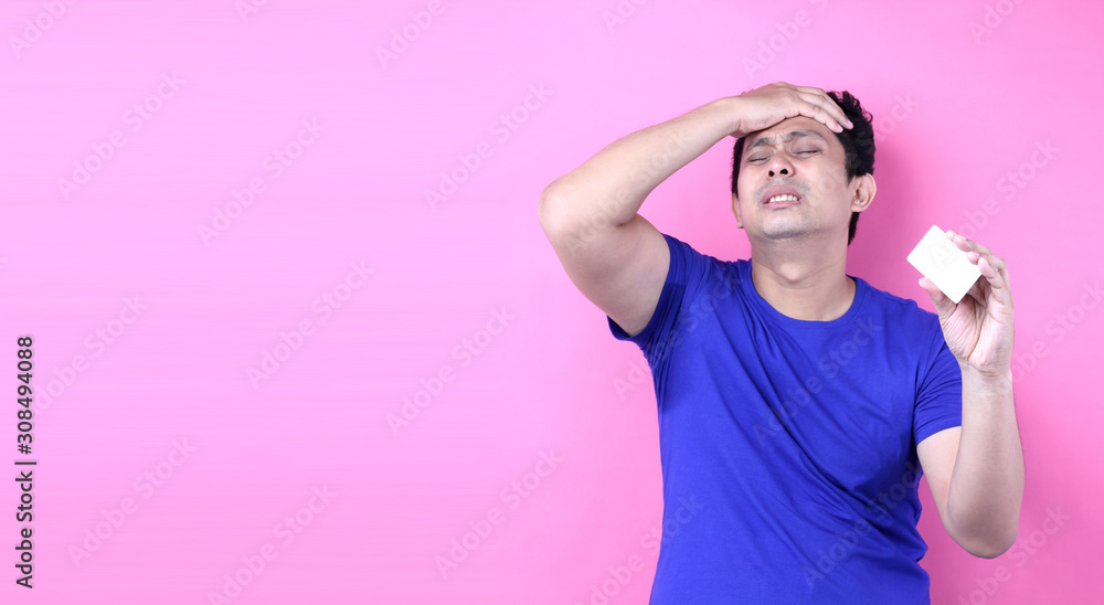 Young handsome Asia man holding credit card space scared in shock with a surprise face, afraid and excited with fear expression on pink background in studio With copy space. Young handsome Asia man holding credit card space scared in shock with a surprise face, afraid and excited with fear expression on pink background in studio With copy space.