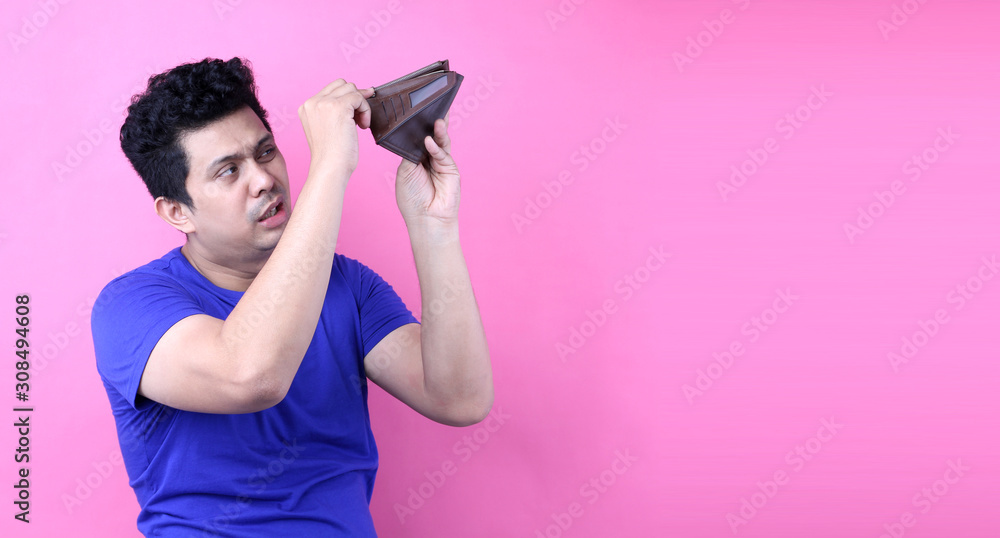 A close-up portrait of a shocked, surprised speechless man asia, holding an empty wallet on pink background in studio With copy space. A close-up portrait of a shocked, surprised speechless man asia, holding an empty wallet on pink background in studio With copy space.