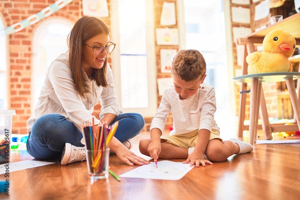 Beautiful teacher and toddler drawing using pencils and paper around lots of toys at kindergarten Beautiful teacher and toddler drawing using pencils and paper around lots of toys at kindergarten