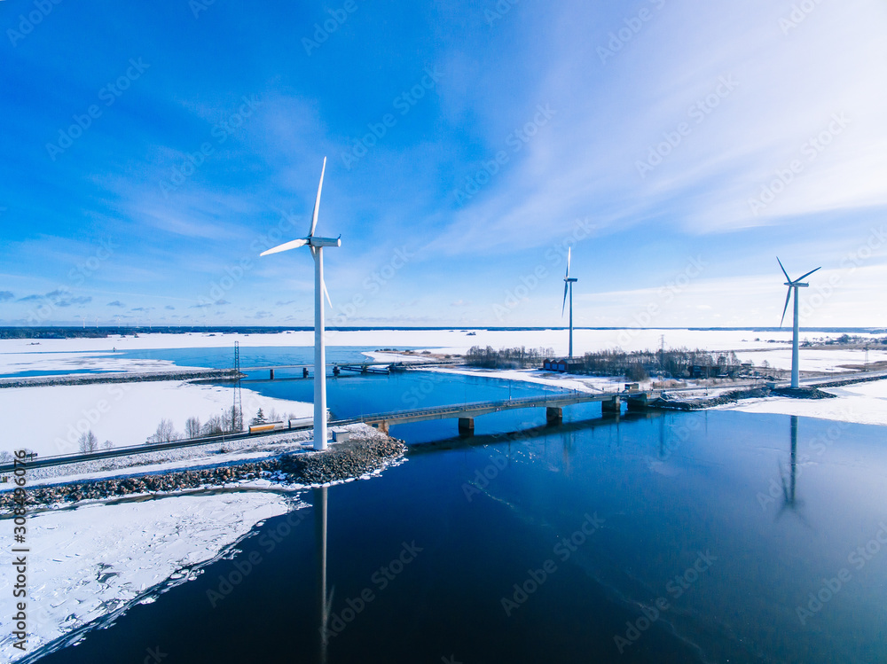 Aerial view of windmills with blue frozen river in snow winter Finland. Wind turbines for electric power