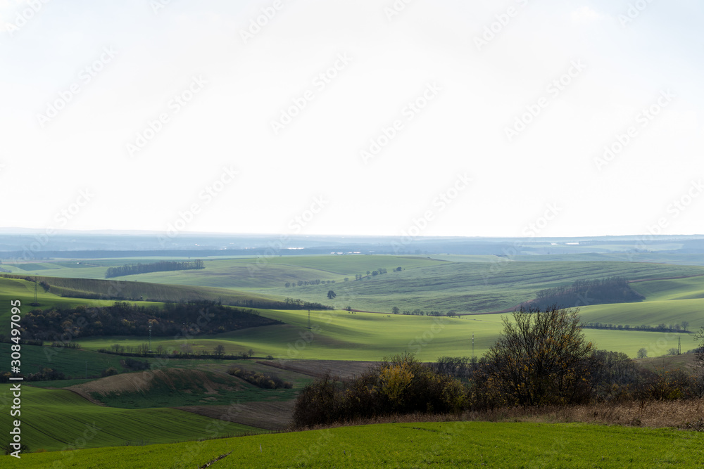 View of vineyards and farms in the Svatoborice region of Moravian Tuscany during a sunny autumn day in the background blue sky full of clouds and rugged wavy landscape full of green color.