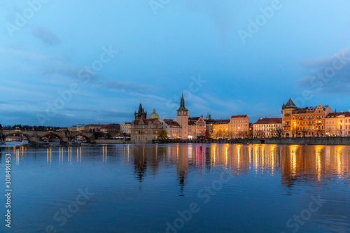 The center of Prague Czech Republic and its biggest landmark on the Vltava river Charles Bridge and the beautiful waterfront illuminated during Christmas at sunset with reflections of lights.