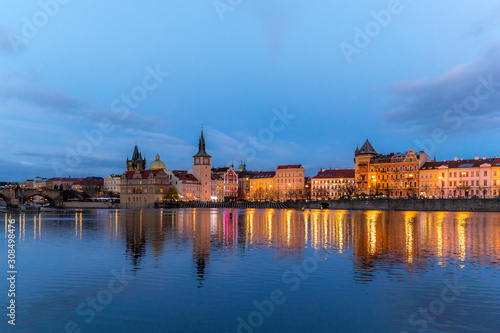 The center of Prague Czech Republic and its biggest landmark on the Vltava river Charles Bridge and the beautiful waterfront illuminated during Christmas at sunset with reflections