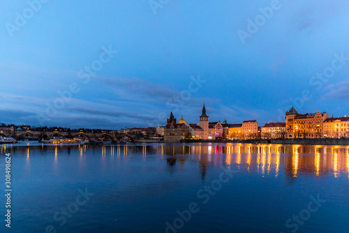 The center of Prague Czech Republic and its biggest landmark on the Vltava river Charles Bridge and the beautiful waterfront illuminated during Christmas at sunset with reflections of lights.