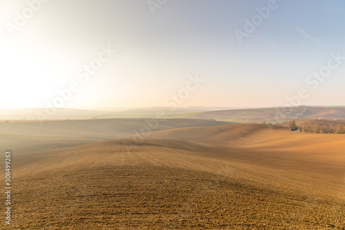 View of plowed land after the season in the Moravian Tuscany region's landscape full of ripples overlooking the village in the background during an afternoon sunny day without clouds