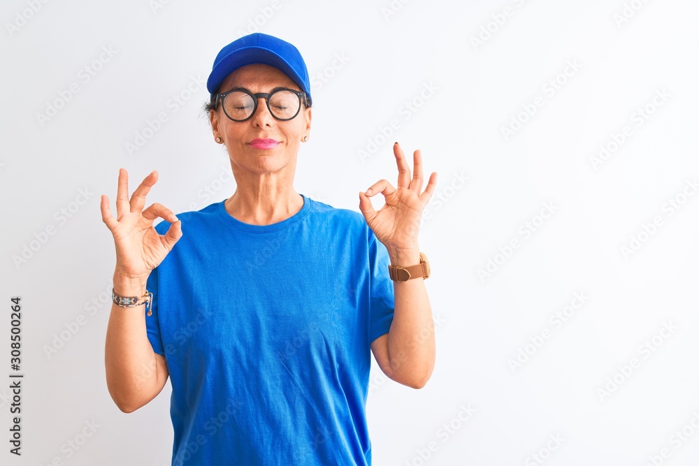 Senior deliverywoman wearing cap and glasses standing over isolated white background relax and smiling with eyes closed doing meditation gesture with fingers. Yoga concept.