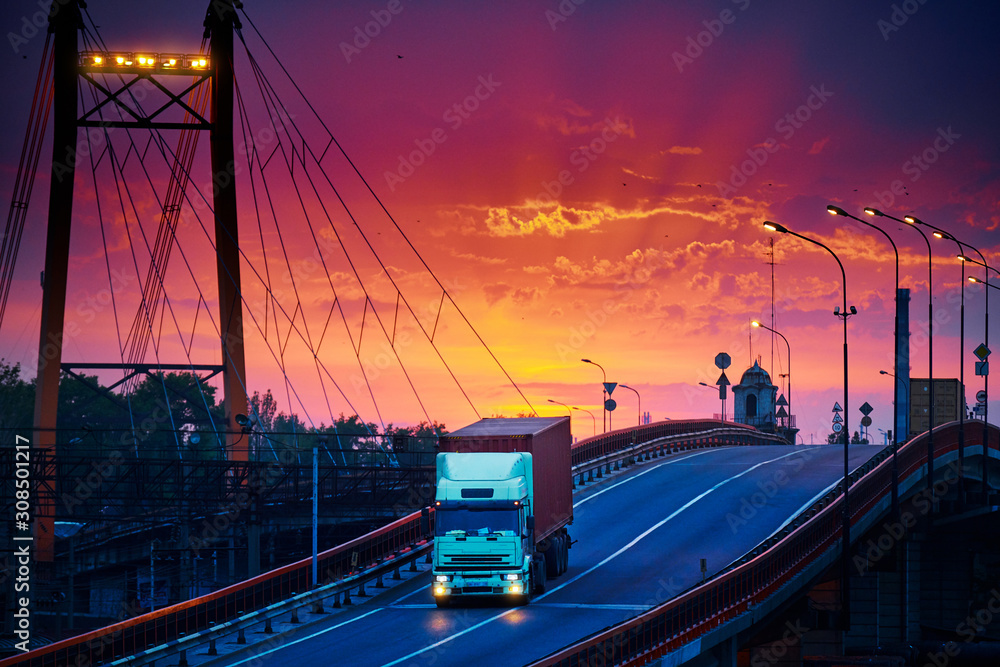 truck with container rides over the bridge, beautiful sunset, freight cars in industrial seaport, the road goes up