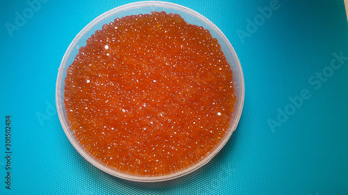Plastic container with red salmon or keta fish caviar on blue background.