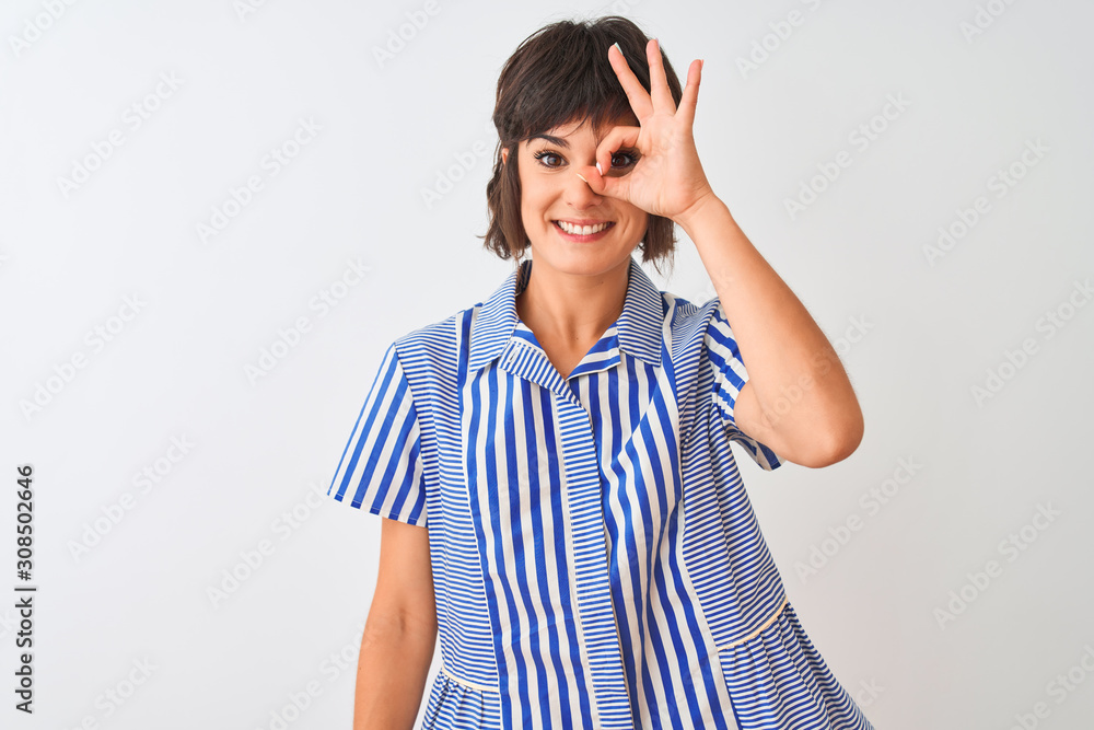 Young beautiful woman wearing blue striped shirt standing over isolated white background doing ok gesture with hand smiling, eye looking through fingers with happy face. Young beautiful woman wearing blue striped shirt standing over isolated white background doing ok gesture with hand smiling, eye looking through fingers with happy face.