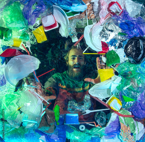 Man drowning in water under plastic recipients pile, garbage. Used bottles and packs filling world ocean killing people. Ecology, environment concept, plastic and glass pollution, nature disaster.