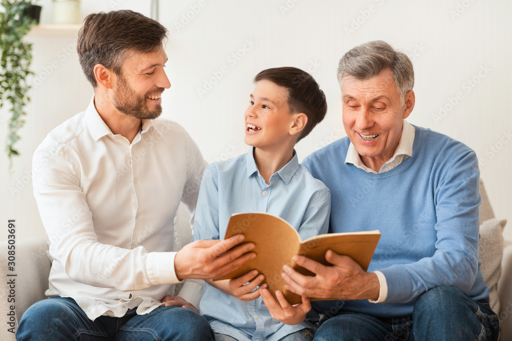 Boy Reading Book Sitting With Father And Grandfather On Sofa Boy Reading Book Sitting With Father And Grandfather On Sofa