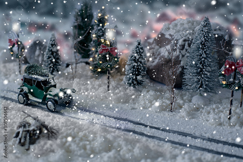 Miniature classic car carrying a christmas tree on snowy road in winter