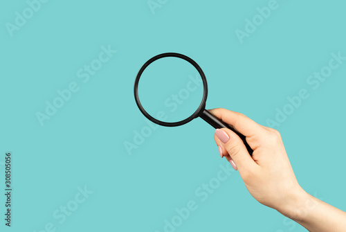 Hand holding magnifying glass on cyan background