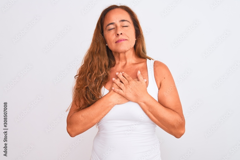 Obraz premium Middle age mature woman standing over white isolated background smiling with hands on chest with closed eyes and grateful gesture on face. Health concept.