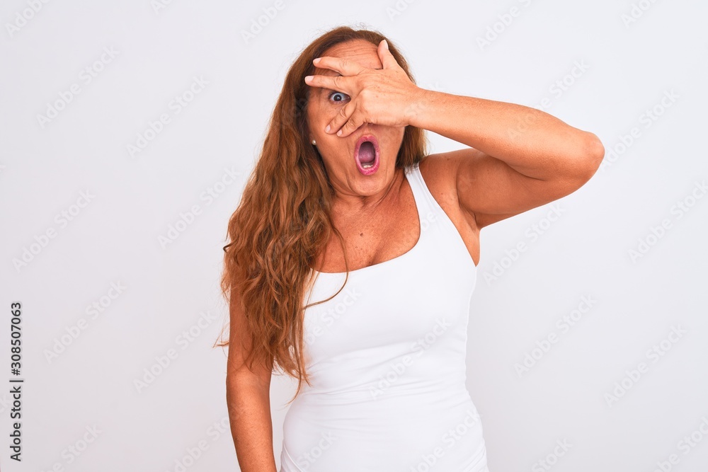 Middle age mature woman standing over white isolated background peeking in shock covering face and eyes with hand, looking through fingers with embarrassed expression. Middle age mature woman standing over white isolated background peeking in shock covering face and eyes with hand, looking through fingers with embarrassed expression.