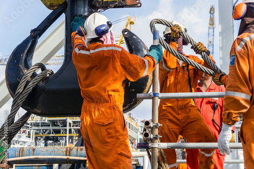 Offshore workers installing a heavy lifting sling onto a crane hook on board a construction work barge at oil field photo