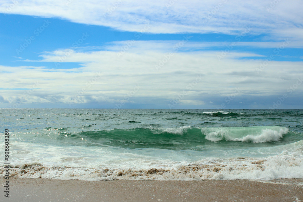 Atlantic ocean, green water, waves, ocean foam, wet sand, white clouds, blue bright saturated sky, Portugal