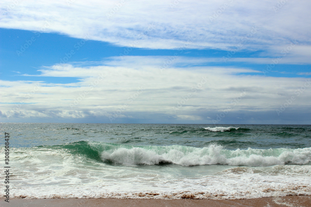 Fototapeta premium Atlantic ocean, green water, waves, ocean foam, wet sand, white clouds, blue bright saturated sky, Portugal