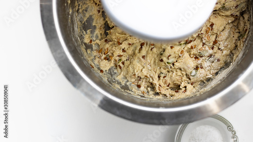 raw sour dough whole wheat bread with seeds, prosess of mixing pastry in metal bowl, knead, horizontal with copy space, selectuve focus, healthy food, nutritious. Top view. White background