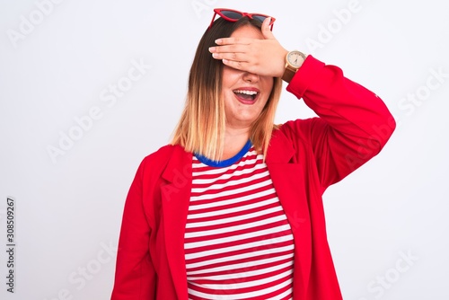 Young beautiful woman wearing striped t-shirt and jacket over isolated white background smiling and laughing with hand on face covering eyes for surprise. Blind concept.