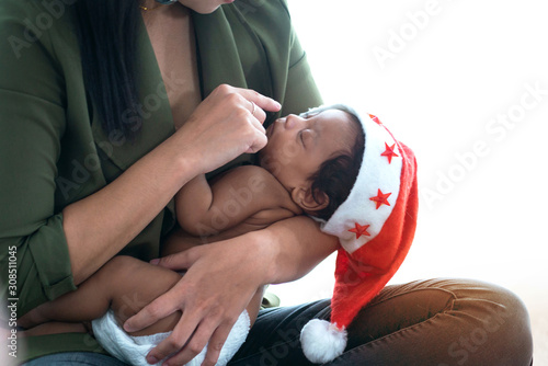 Mother plays with dark-skinned baby by touching fingers with nose, baby wearing a Santa hat, the love bond between mother and child