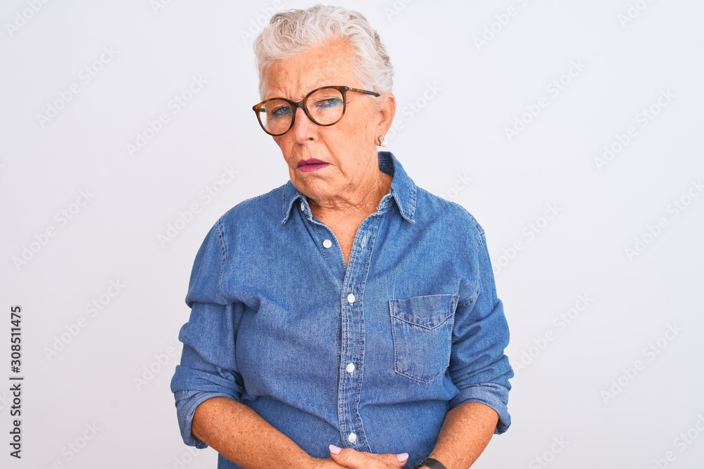 Senior grey-haired woman wearing denim shirt and glasses over isolated white background looking sleepy and tired, exhausted for fatigue and hangover, lazy eyes in the morning. Senior grey-haired woman wearing denim shirt and glasses over isolated white background looking sleepy and tired, exhausted for fatigue and hangover, lazy eyes in the morning.