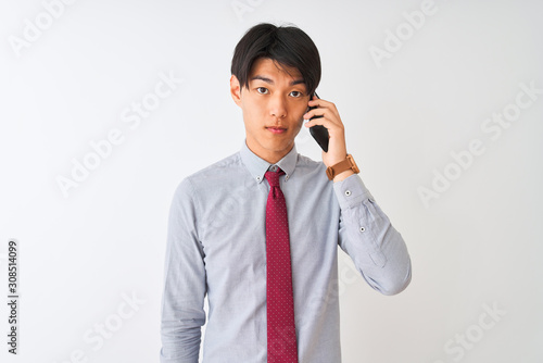 Chinese businessman wearing tie talking on the smartphone over isolated white background with a confident expression on smart face thinking serious