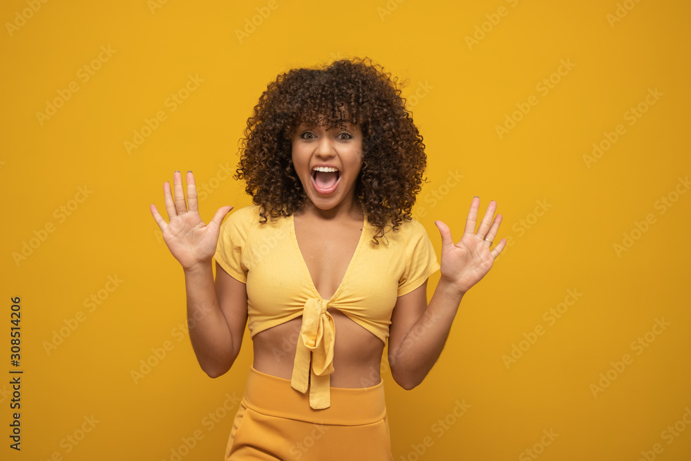 Girl with a surprise expression on her face with arms up. Yellow background. Girl with a surprise expression on her face with arms up. Yellow background.