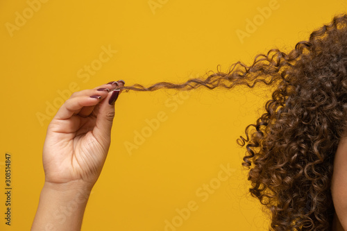 Close-up American African woman pulling a lock of hair. Curly hair on yellow background. photo