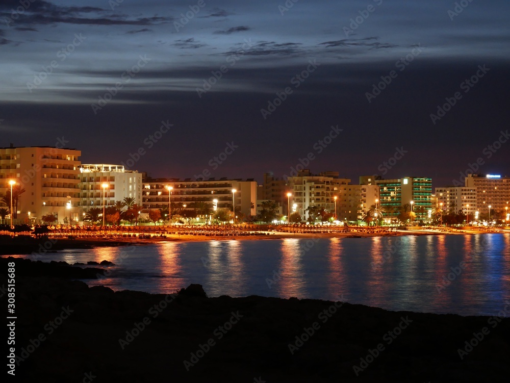 Night view of the coastline, sea and beach with glowing reflective lights at Cala Millor, Majorca