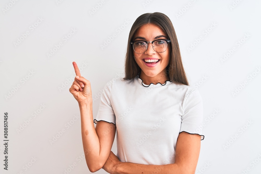 Young beautiful woman wearing casual t-shirt and glasses over isolated white background with a big smile on face, pointing with hand and finger to the side looking at the camera. Young beautiful woman wearing casual t-shirt and glasses over isolated white background with a big smile on face, pointing with hand and finger to the side looking at the camera.