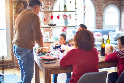 Beautiful family smiling happy and confident. One of them curving roasted turkey celebrating christmas at home