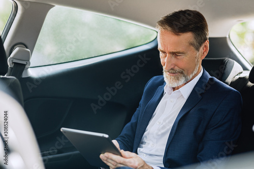 Senior entrepreneur typing on a digital tablet while sitting on the backseat in taxi © Artem Varnitsin