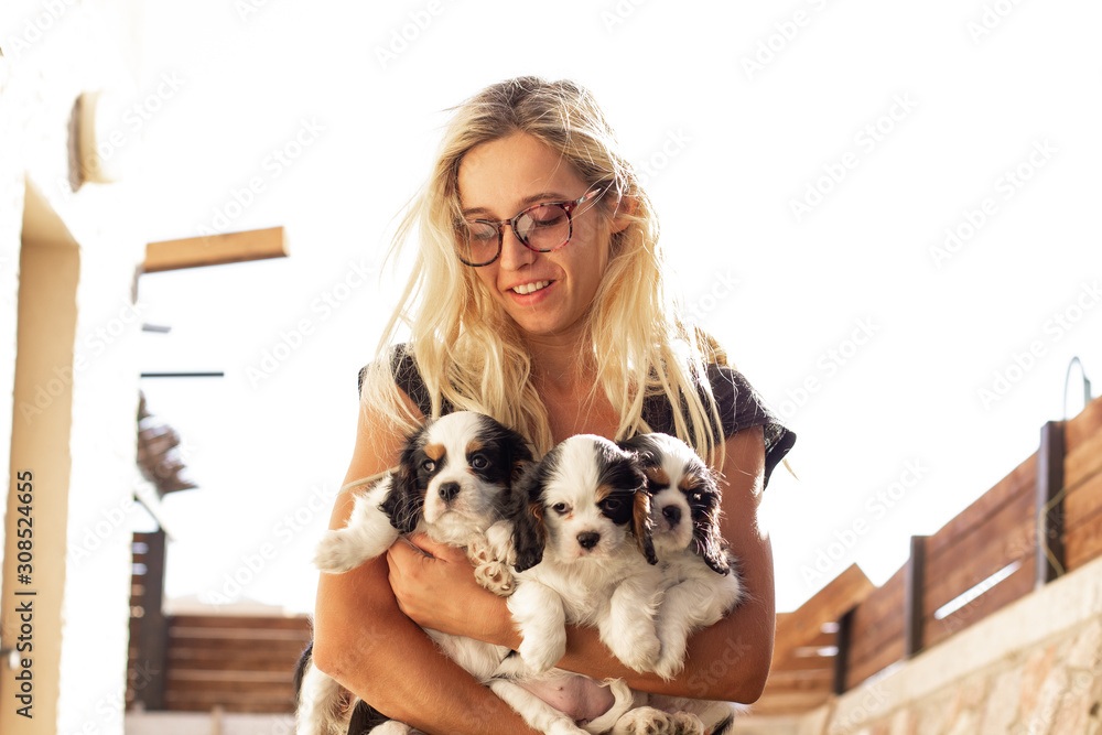 glad woman without make up with King Charles Cavalier puppies in hugs 