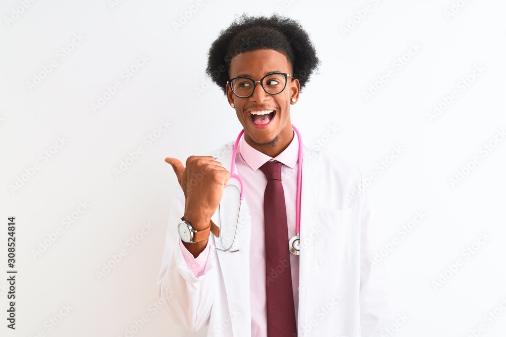 Young african american doctor man wearing pink stethoscope over isolated white background smiling with happy face looking and pointing to the side with thumb up. Young african american doctor man wearing pink stethoscope over isolated white background smiling with happy face looking and pointing to the side with thumb up.