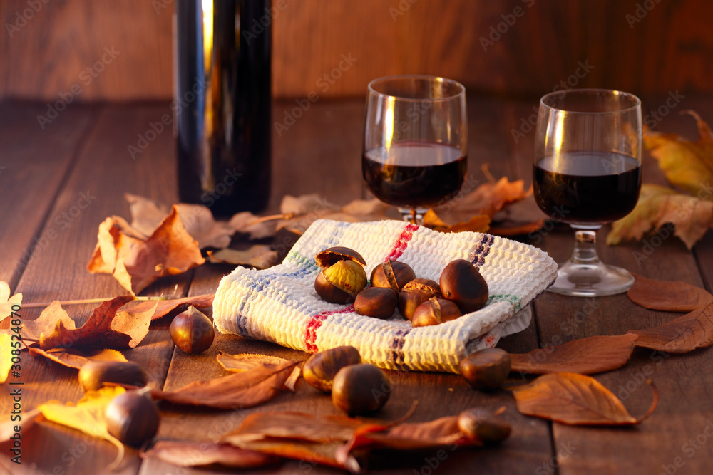 an autumn time still life with a bottle and a glass of red wine and roasted chestnuts wrapped in an old dish towel