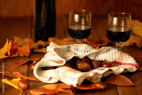 an autumn time still life with a bottle and a glass of red wine and roasted chestnuts wrapped in an old dish towel