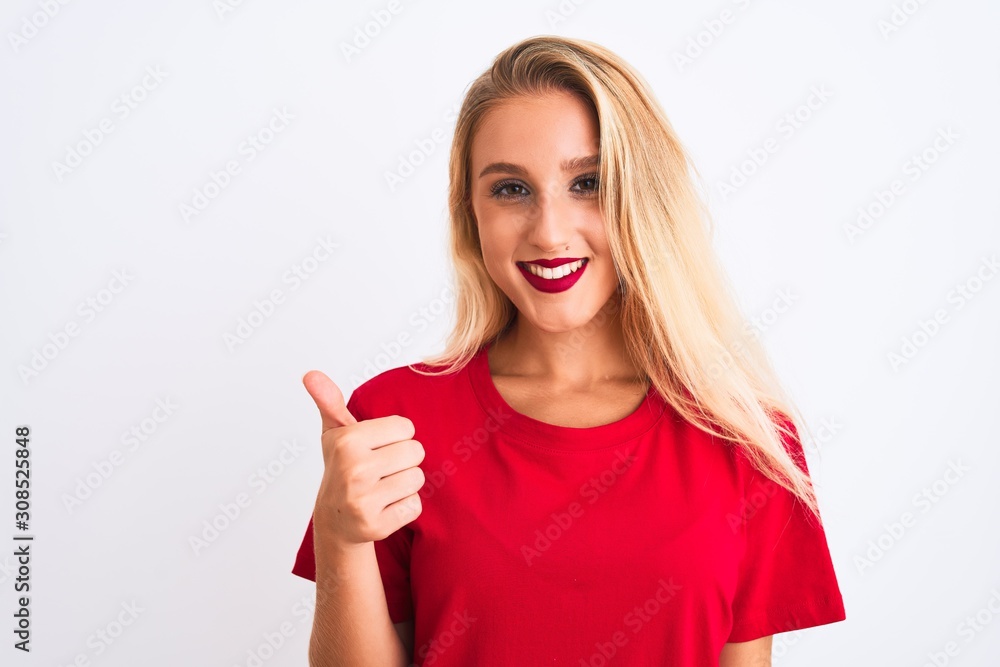 Young beautiful woman wearing red casual t-shirt standing over isolated white background doing happy thumbs up gesture with hand. Approving expression looking at the camera with showing success. Young beautiful woman wearing red casual t-shirt standing over isolated white background doing happy thumbs up gesture with hand. Approving expression looking at the camera with showing success.