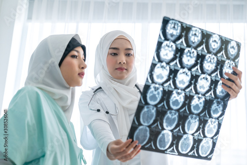 Woman muslim doctors shows at an X-ray of the found problem of patient and explains the cause of her pain.