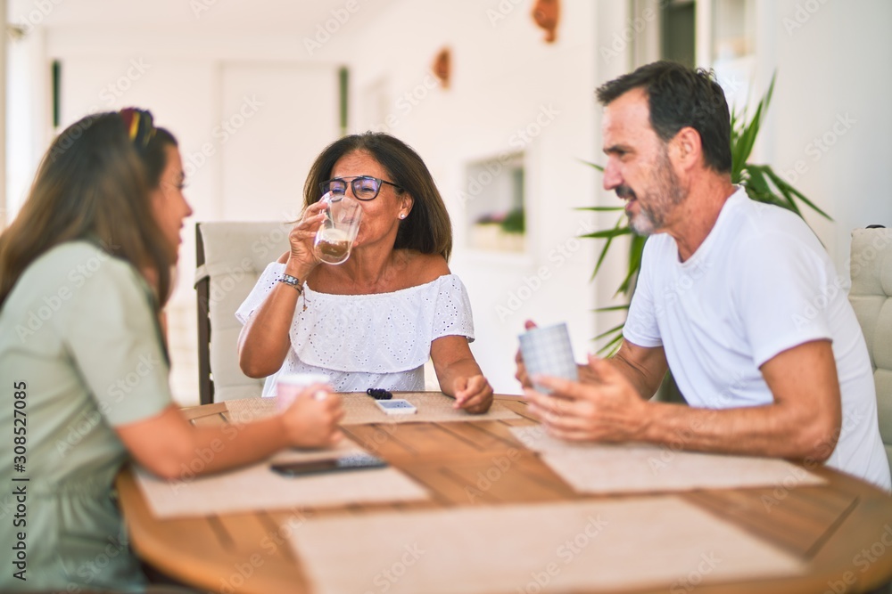 Fototapeta premium Beautiful family sitting on terrace drinking cup of coffee speaking and smiling