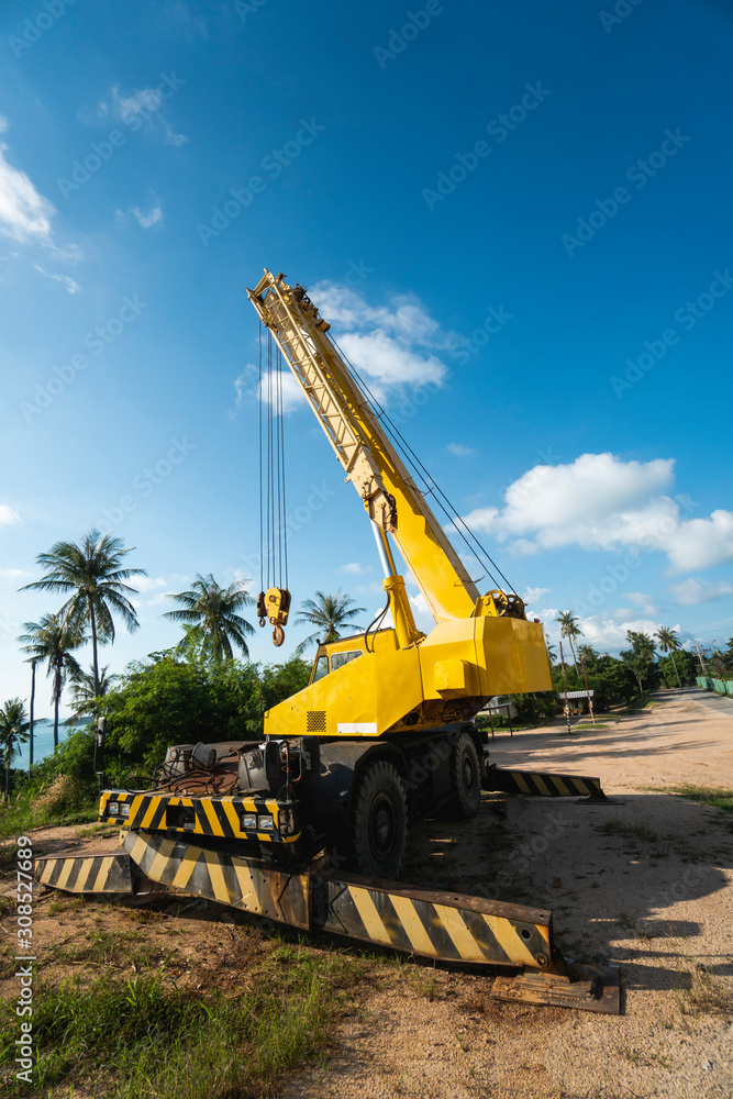 Yellow automobile crane with risen telescopic boom outdoors. Mobile construction crane on a constructin site. Crane machine stand by waiting for work under the construction building. Heavy industry. Yellow automobile crane with risen telescopic boom outdoors. Mobile construction crane on a constructin site. Crane machine stand by waiting for work under the construction building. Heavy industry.