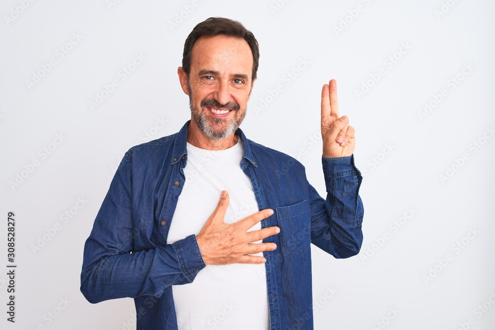 Middle age handsome man wearing blue denim shirt standing over isolated white background smiling swearing with hand on chest and fingers up, making a loyalty promise oath Middle age handsome man wearing blue denim shirt standing over isolated white background smiling swearing with hand on chest and fingers up, making a loyalty promise oath
