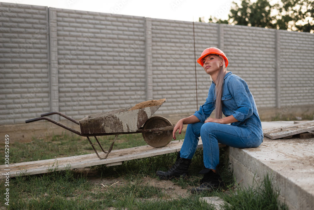 A woman in an orange helmet sits on a construction site